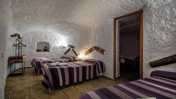 A rustic room with three beds, a stone floor, and a white textured ceiling.