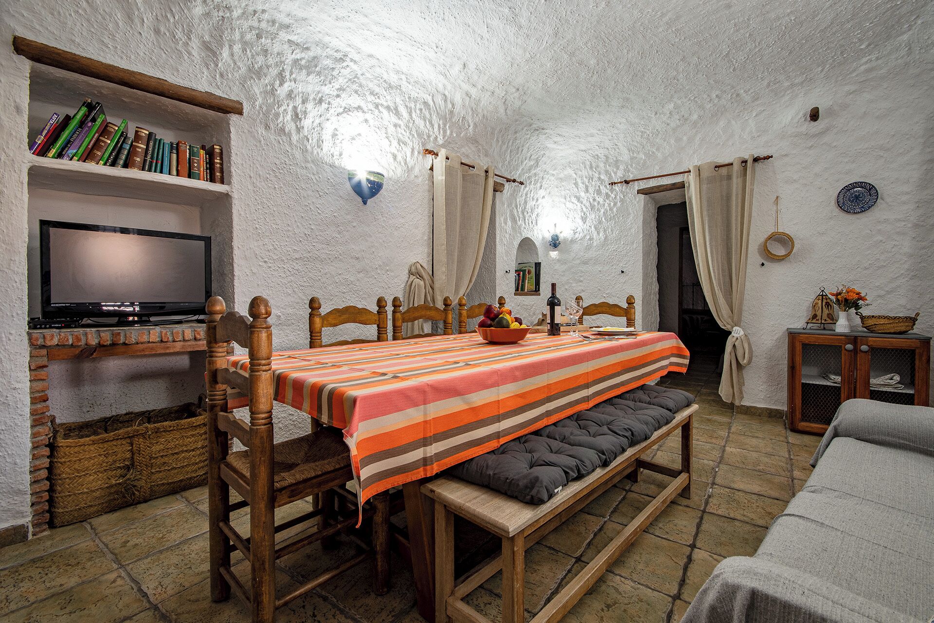 A cozy room with a wooden table set for dining, a television on a shelf, and a bookshelf filled with books.