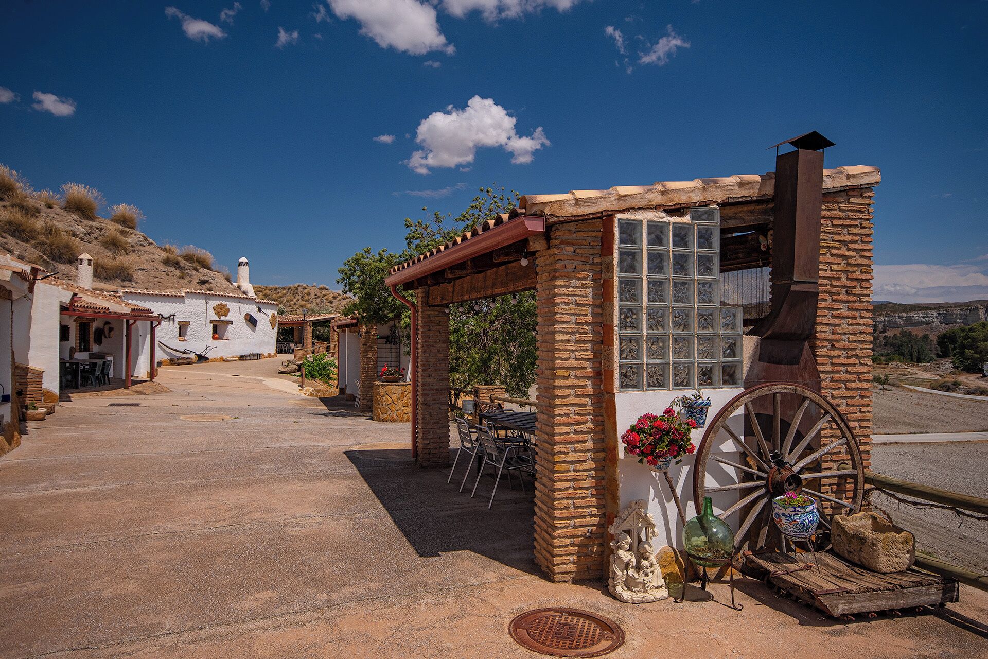 Un área de estar al aire libre de estilo rústico con un arco de piedra, una rueda de madera grande y una planta en maceta.