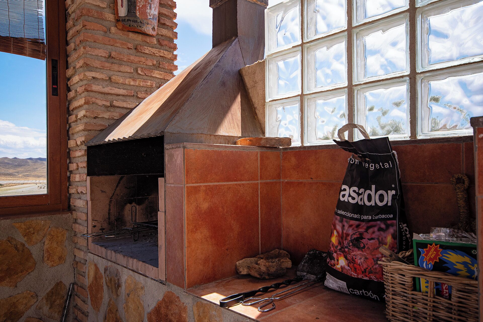 Una cocina rústica con chimenea de ladrillo, un ventanal con vistas a las montañas y un saco de carbón.