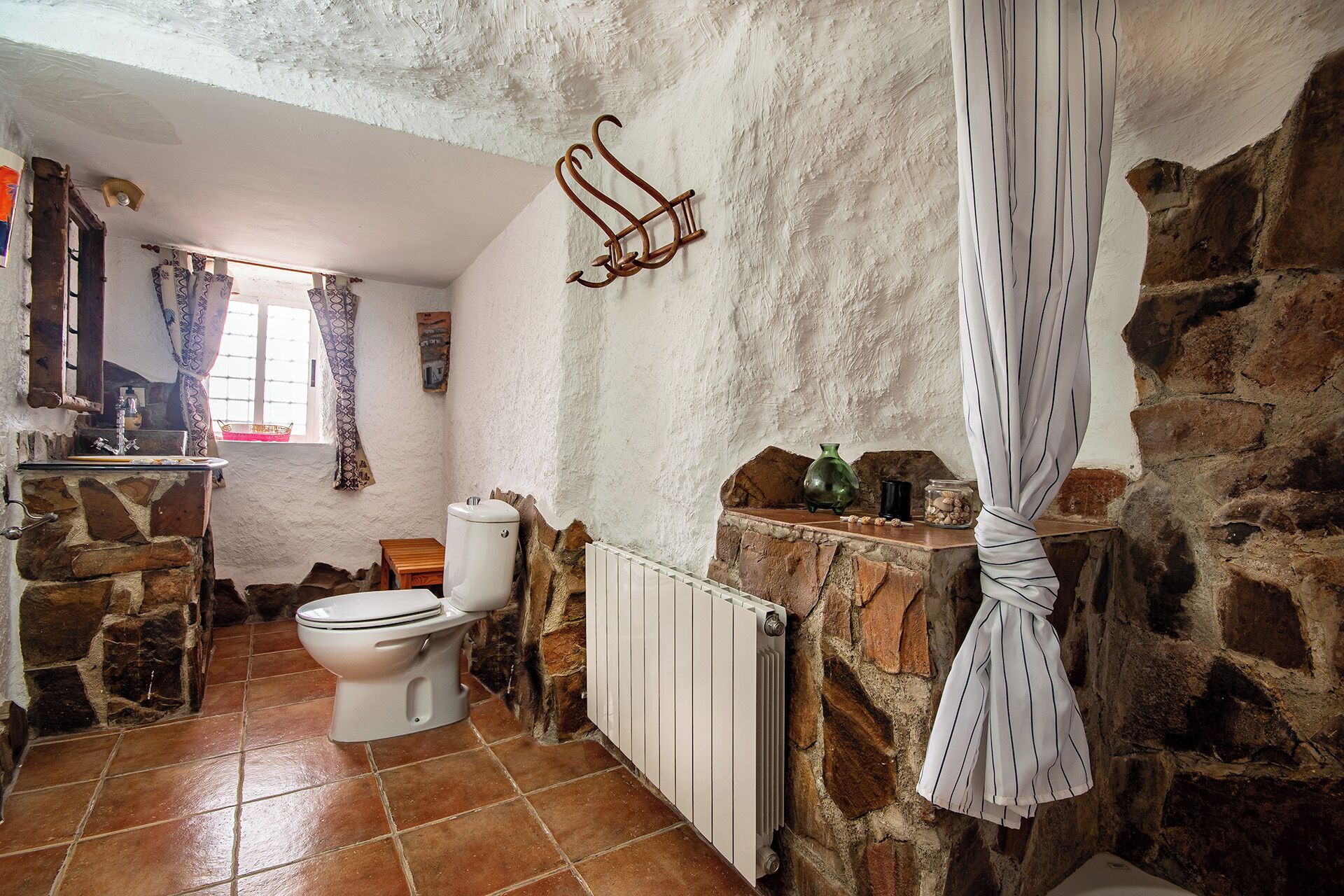 Un baño rústico con pared de piedra, inodoro blanco, radiador y cortina de ducha colgante.
