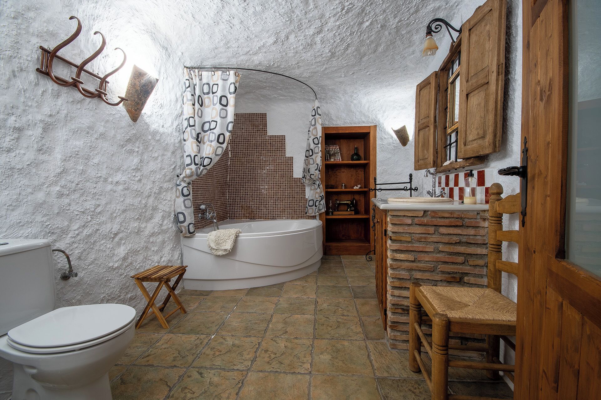 Een rustieke badkamer met een badkuip, houten planken, een houten stoel en een wit toilet.