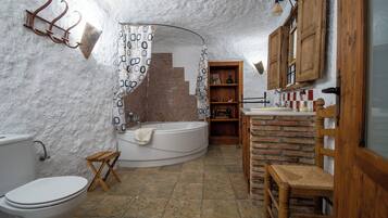 Een rustieke badkamer met een badkuip, houten planken, een houten stoel en een wit toilet.