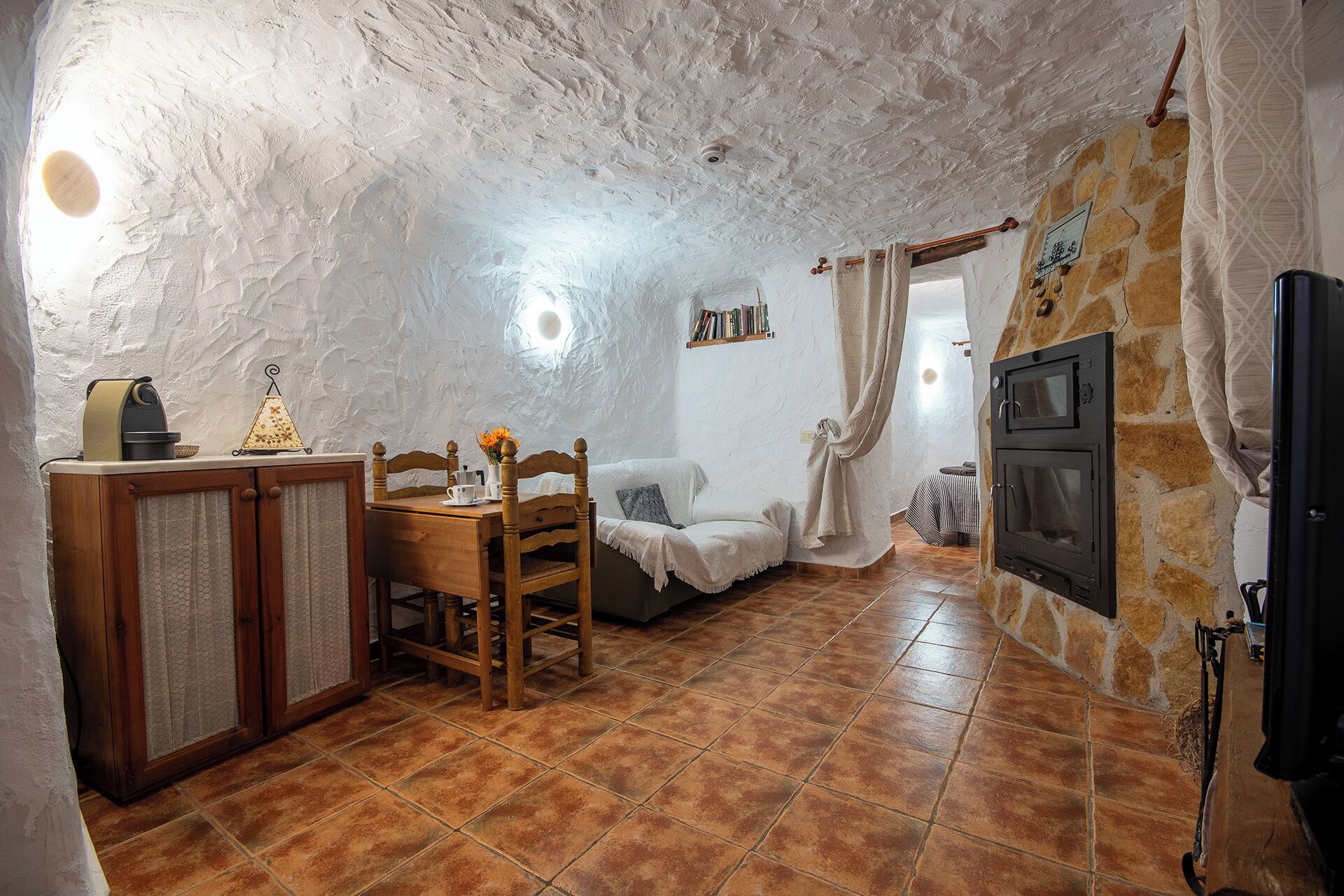 A rustic stone interior with a wooden dining table, a cozy seating area, and a fireplace.