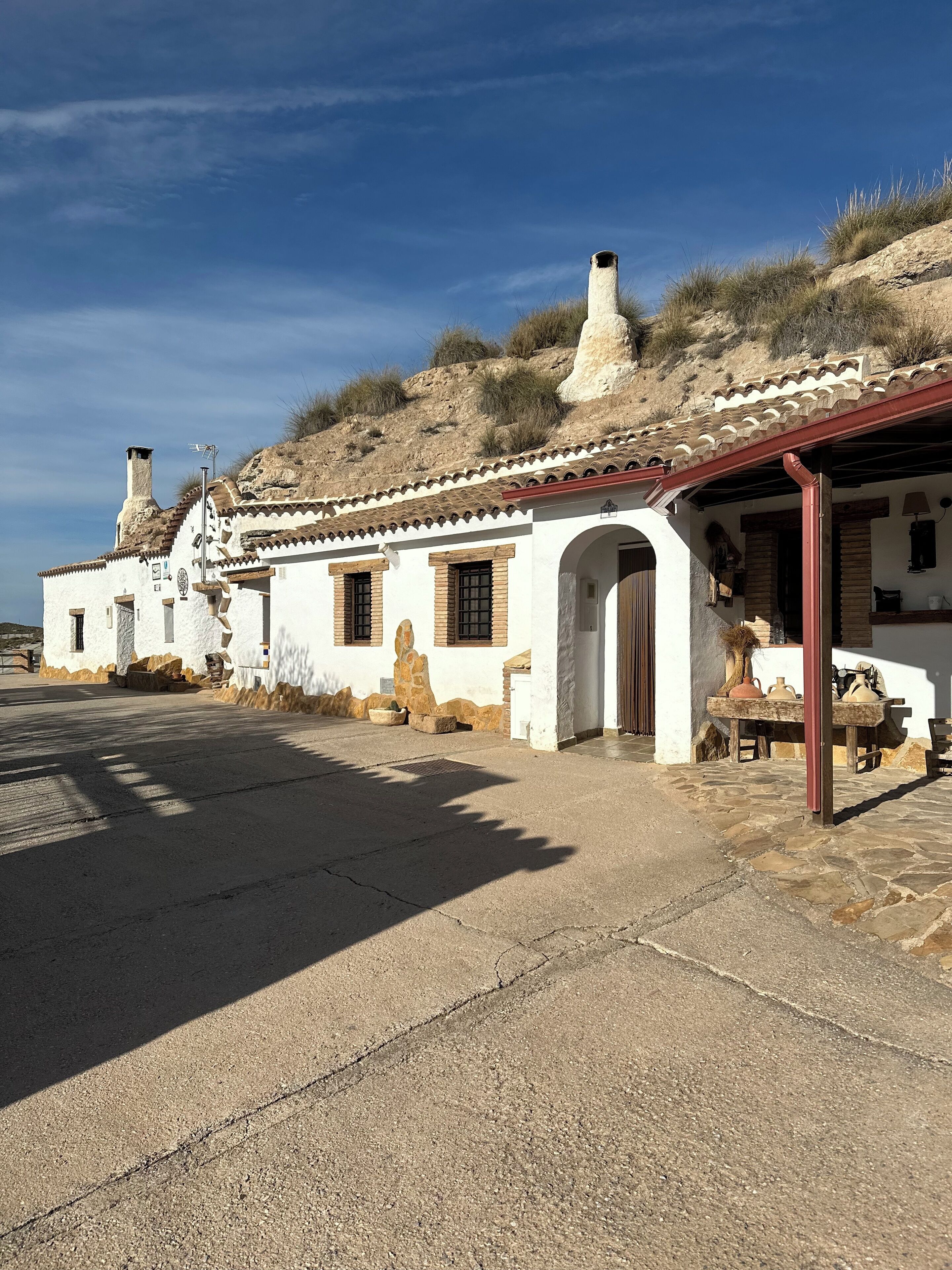 A traditional white building with a tiled roof, stone walls, and a small porch area with a table and chairs.