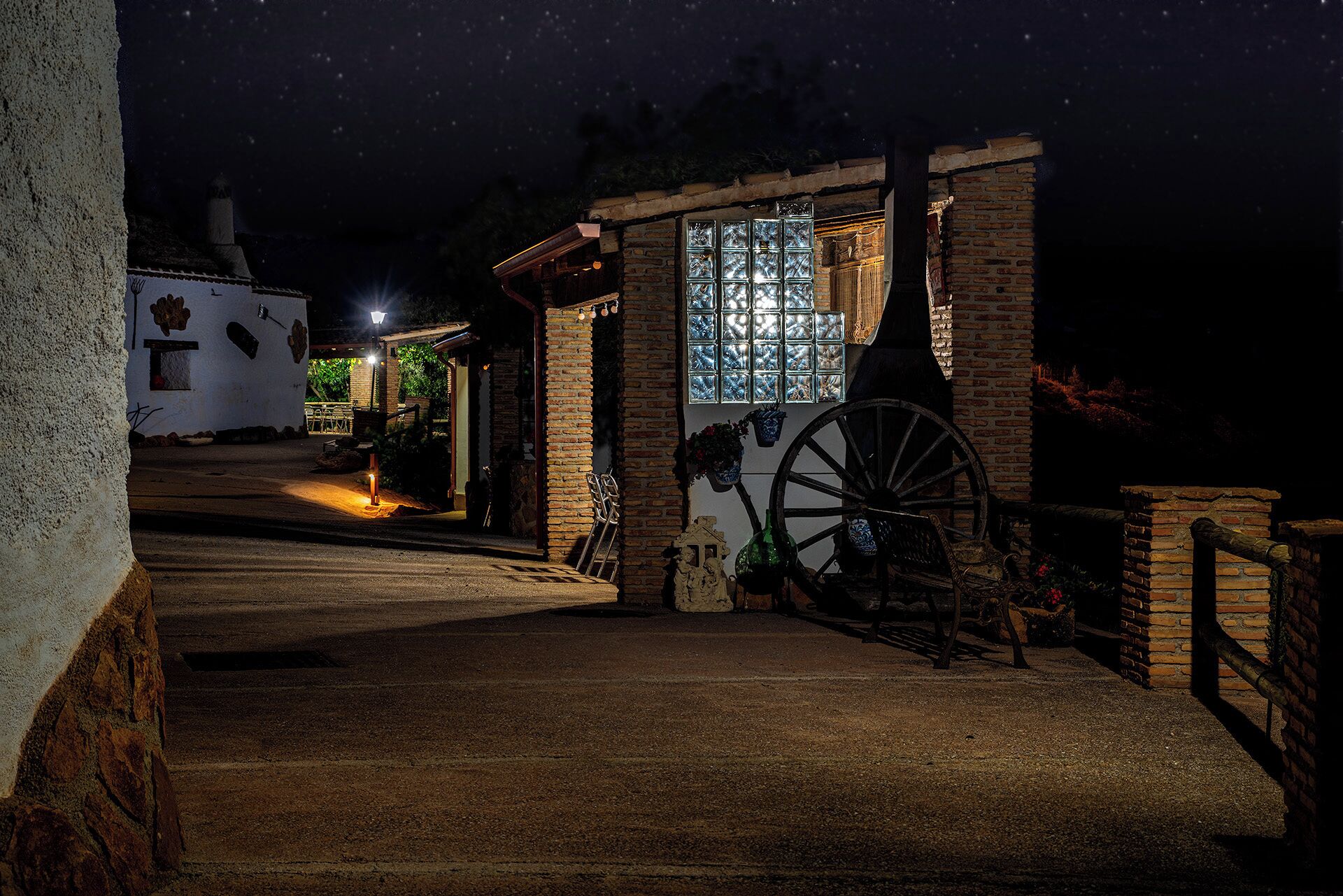 A rustic building with a large wooden wheel, a stone wall, and a lit window.