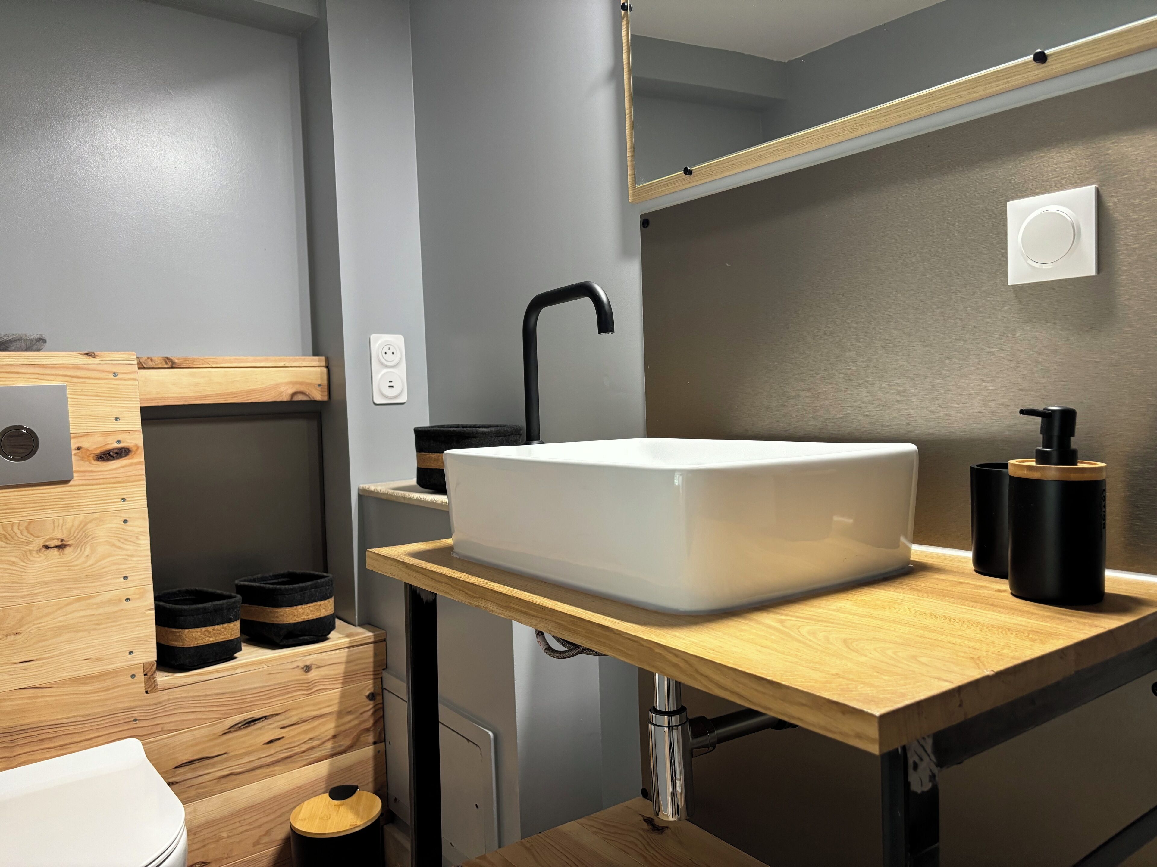 Een moderne badkamer met een houten wastafelmeubel, een witte wastafel en een spiegel erboven.