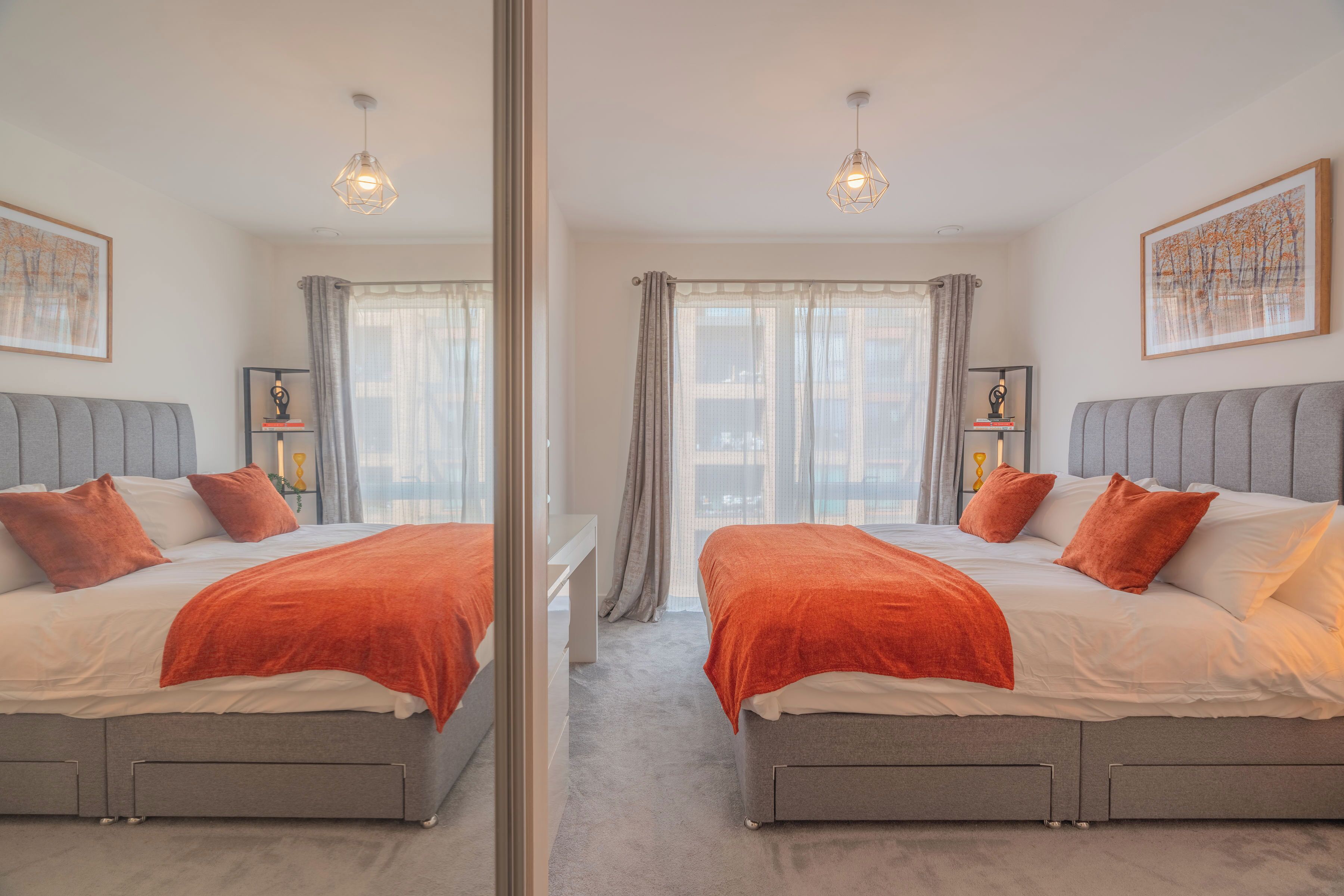 Ein Zimmer mit Spiegel, zwei Betten, grauen Kopfteilen, weißer Bettwäsche und orangen Zierkissen.