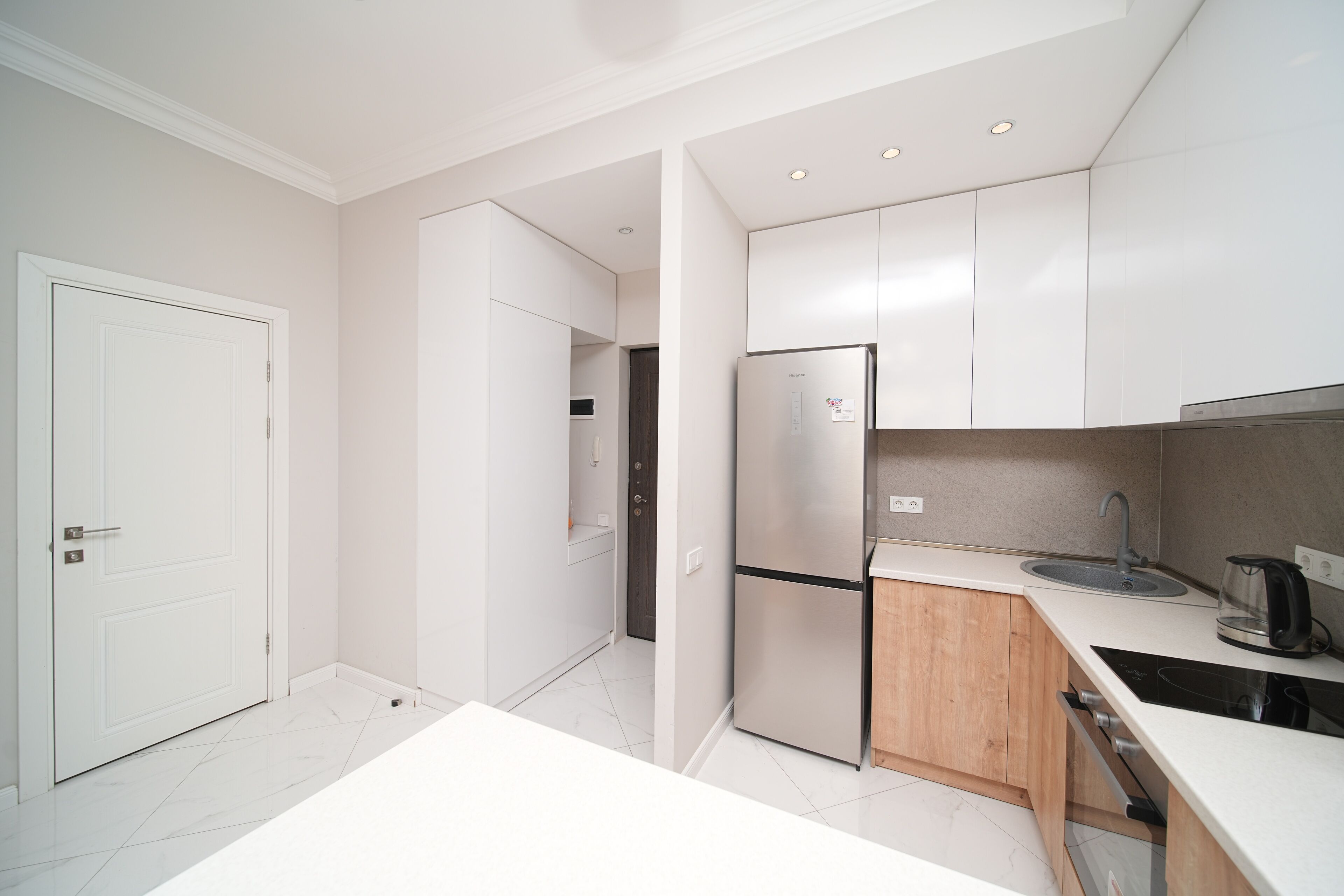 A modern kitchen with white cabinets, a stainless steel refrigerator, a sink, and a stove.