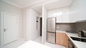 A modern kitchen with white cabinets, a stainless steel refrigerator, a sink, and a stove.