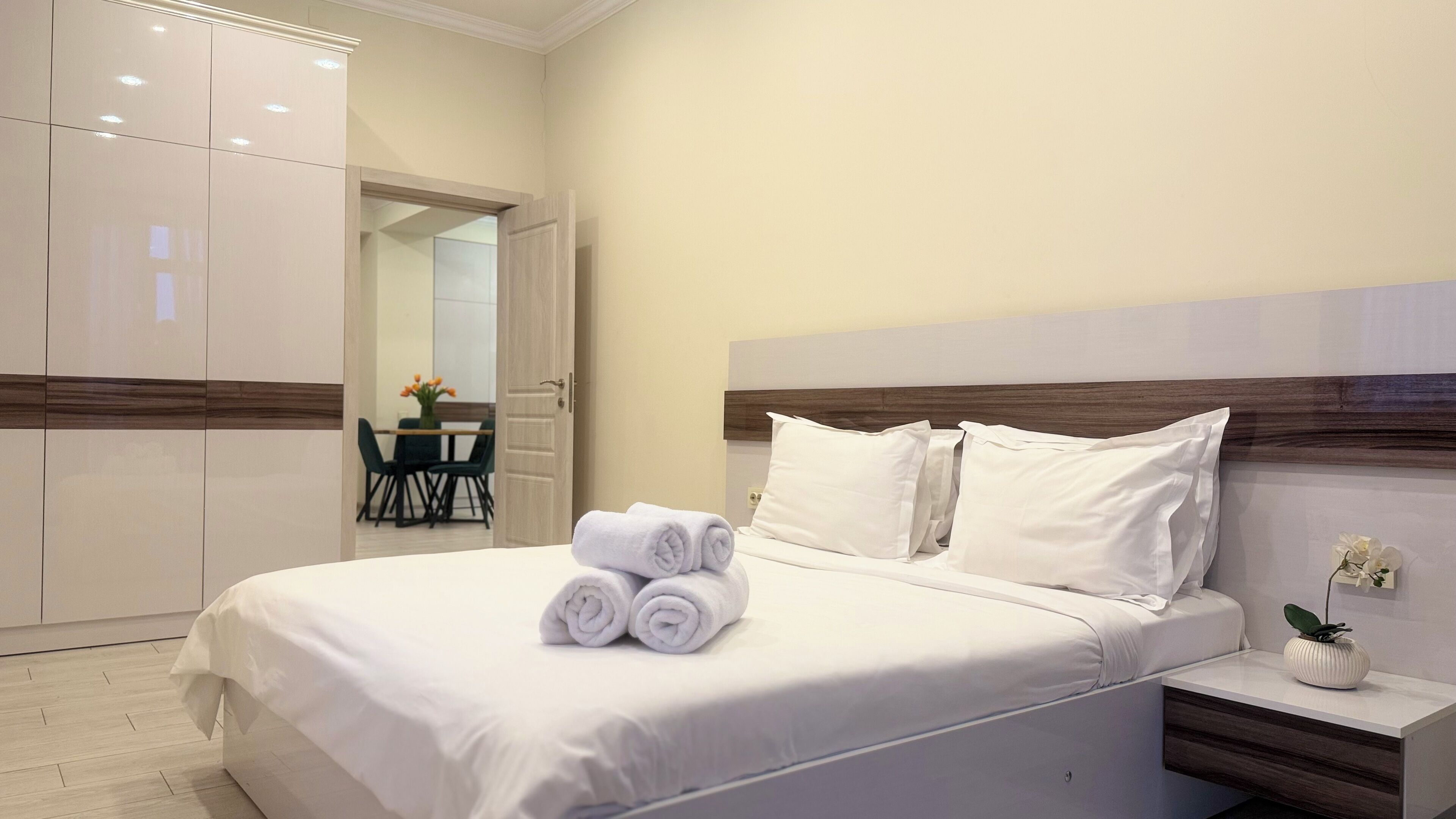 Habitación de hotel con una cama bien hecha, un cabecero de madera y una mesita de noche con un florero.