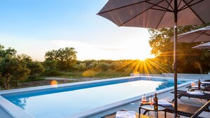 Ein Pool mit Liegestühlen und Sonnenschirmen, umgeben von viel Grün.