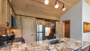 A kitchen with a granite countertop, stainless steel appliances, wooden cabinets, and pendant lighting. - Cliffside Suite | AC, Pool, Hot Tub, Golf & Ski (Durango)