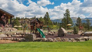 A playground with a slide and swings, surrounded by rocks and trees, with a mountain view in the background. - Cliffside Suite | AC, Pool, Hot Tub, Golf & Ski (Durango)
