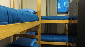 Une chambre avec des lits superposés, dotée de draps bleus, de lits superposés en bois et d’une armoire noire.