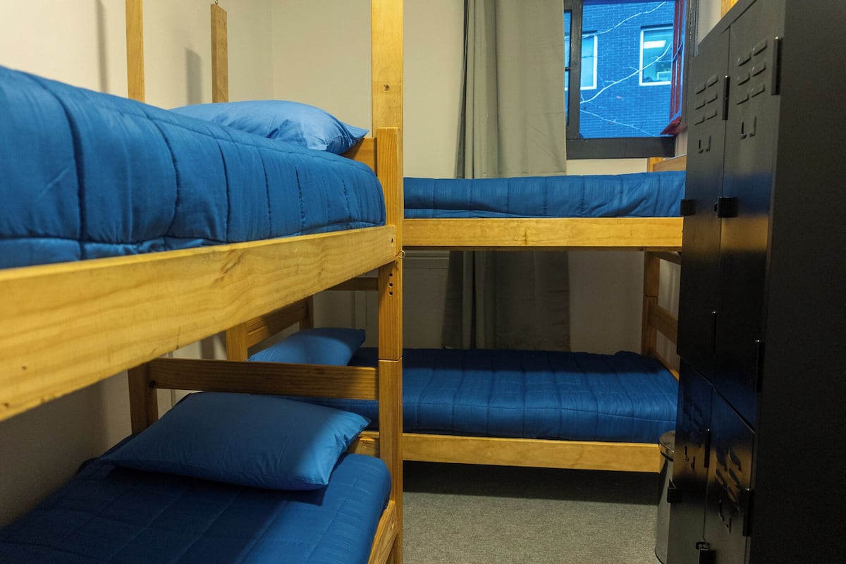 Dormitorio con literas, ropa de cama azul, literas de madera y un armario negro.