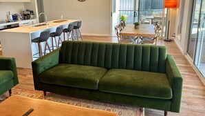 A modern living room with a green sofa, a wooden coffee table, and a kitchen area with bar stools. - House on the hill | Kangaroo lookout (Wodonga)