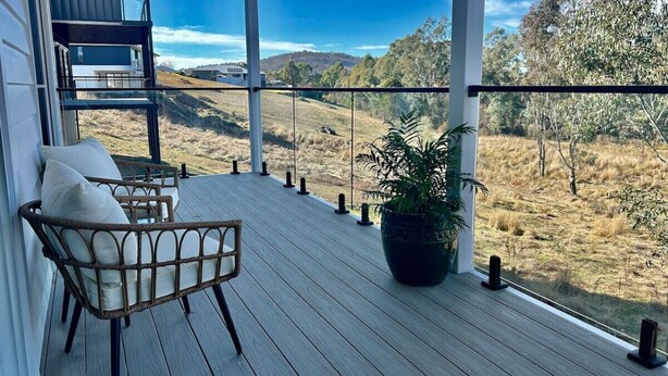 A wooden deck with a wicker chair and a potted plant, overlooking a rural landscape. - House on the hill | Kangaroo lookout (Wodonga)