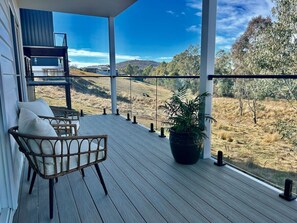 A wooden deck with a wicker chair and a potted plant, overlooking a rural landscape. - House on the hill | Kangaroo lookout (Wodonga)