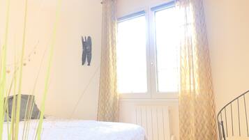 Ein Schlafzimmer mit einem Bett, einem Heizkörper, einem Fenster mit Vorhängen und einer Treppe.