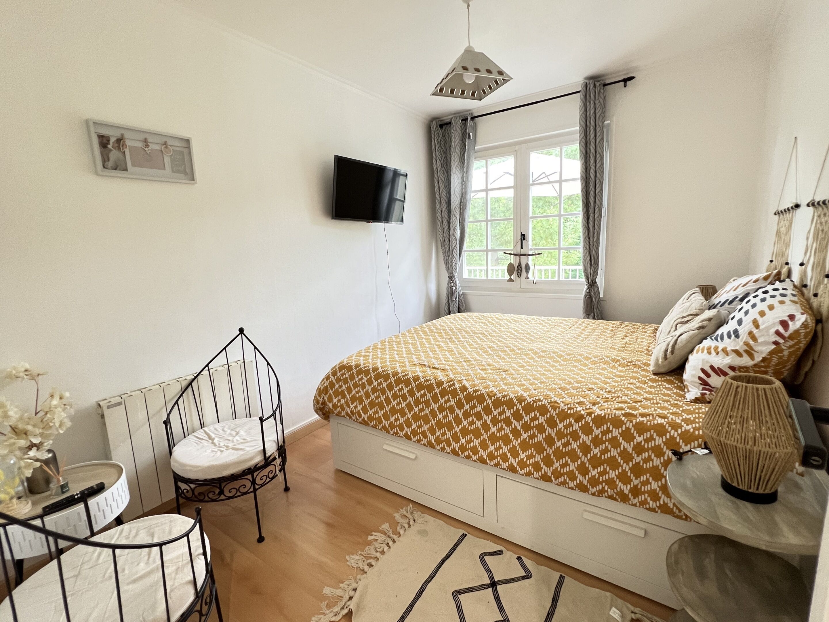Une chambre à coucher avec un lit, une télévision, une fenêtre avec des rideaux, une chaise et une table de chevet.