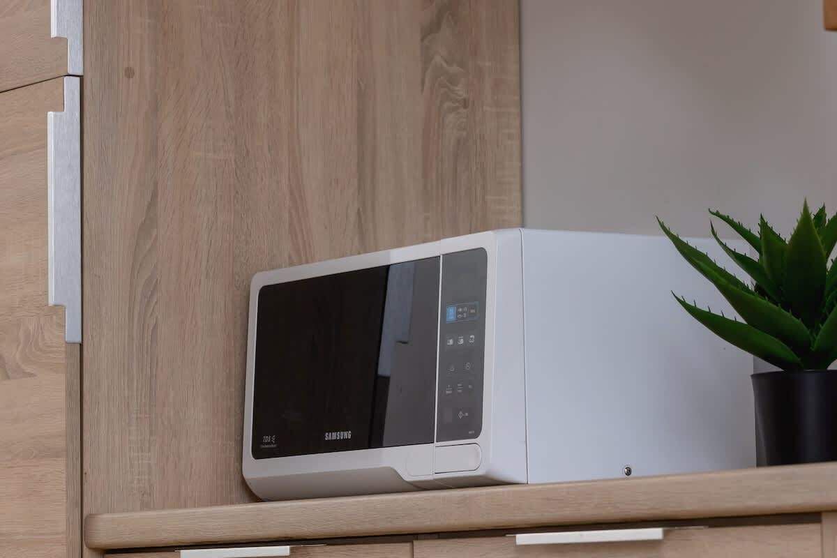 Valkoinen mikroaaltouuni on puuhyllyllä ruukkukasvin vieressä.