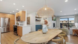 Cozinha moderna com armários de madeira, eletrodomésticos de aço inoxidável e uma sala de jantar com mesa e cadeiras de madeira.