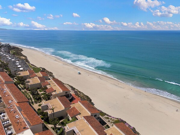A coastal residential area with beachfront properties, including houses with red-tiled roofs and a sandy beach.