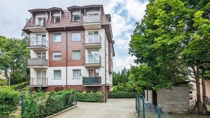 A multi-story residential building with balconies, a paved driveway, and surrounding greenery.
