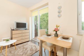 A modern kitchen with a dining area, a TV, and a large window with a view of trees.