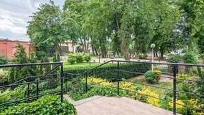 A landscaped garden area with a paved walkway, metal railings, and various green shrubs and trees.