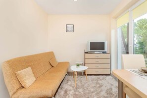 A compact living space with a sofa, a small table, a TV, and a window with a view.
