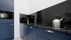 Une cuisine moderne avec des meubles bleu foncé, un plan de travail en marbre noir et des appareils électroménagers en acier inoxydable.