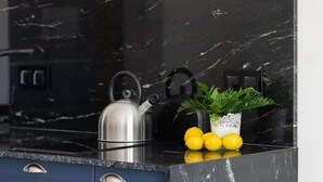 Une cuisine dotée d’un plan de travail en marbre noir, d’une bouilloire en acier inoxydable et d’une plante en pot ornée de citrons jaunes.
