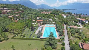 Eine Vogelperspektive zeigt einen luxuriösen Urlaubsort mit einem großen Schwimmbad, üppiger Vegetation und einem See im Hintergrund.