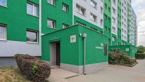 Un edificio residencial de varios pisos con fachada verde y blanca, numerado 9A, y un pequeño acceso con una puerta y un cartel.
