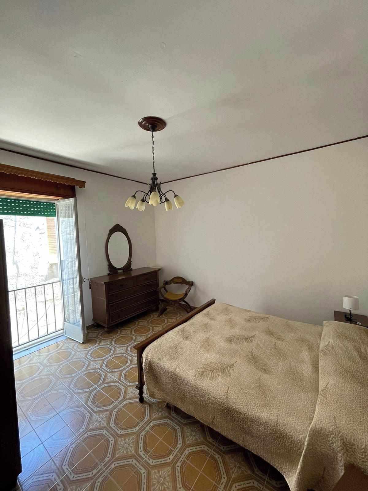 A bedroom with a bed, dresser, chair, and a hanging light fixture.