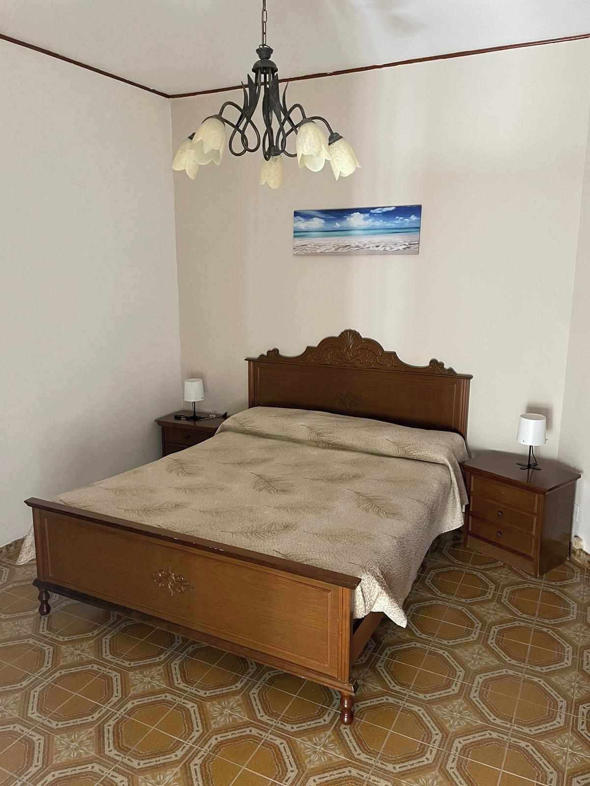 Un dormitorio con una cama de madera, una mesita de noche, una lámpara y un cuadro de una playa.