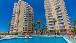 Two high-rise hotels with balconies, a swimming pool with lounge chairs, and palm trees. - Las Americas Ocean view Sunsets (Arona)