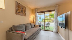 A living room with a sofa, a flat-screen TV, and a view of a garden through a glass door.