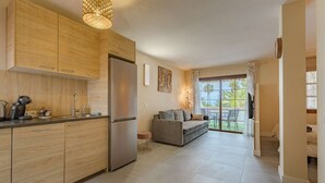 A modern kitchen with wooden cabinets, a stainless steel refrigerator, and a dining area with a sofa and table.
