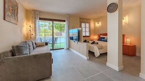 A spacious living area with a sofa, a television, and a bed with a view of the outdoors.