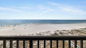 A beach with umbrellas and people, a clear sky, and a railing in the foreground. - Romar House 505B by Liquid Life (Orange Beach)