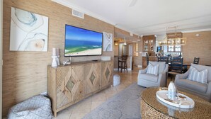 A modern living room with a large flat-screen TV, a wooden cabinet, a dining area with chairs, and a ceiling fan. - Romar House 505B by Liquid Life (Orange Beach)