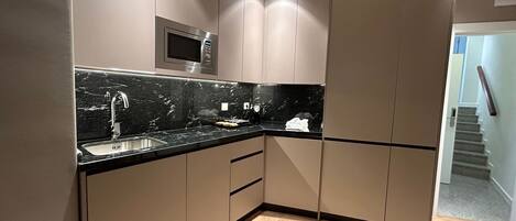 A modern kitchen with a black marble countertop, stainless steel appliances, and wooden flooring.