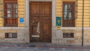 Una amplia puerta doble de madera con una reja metálica, flanqueada por dos ventanas con barrotes, y un letrero que indica "AT Ciudad".