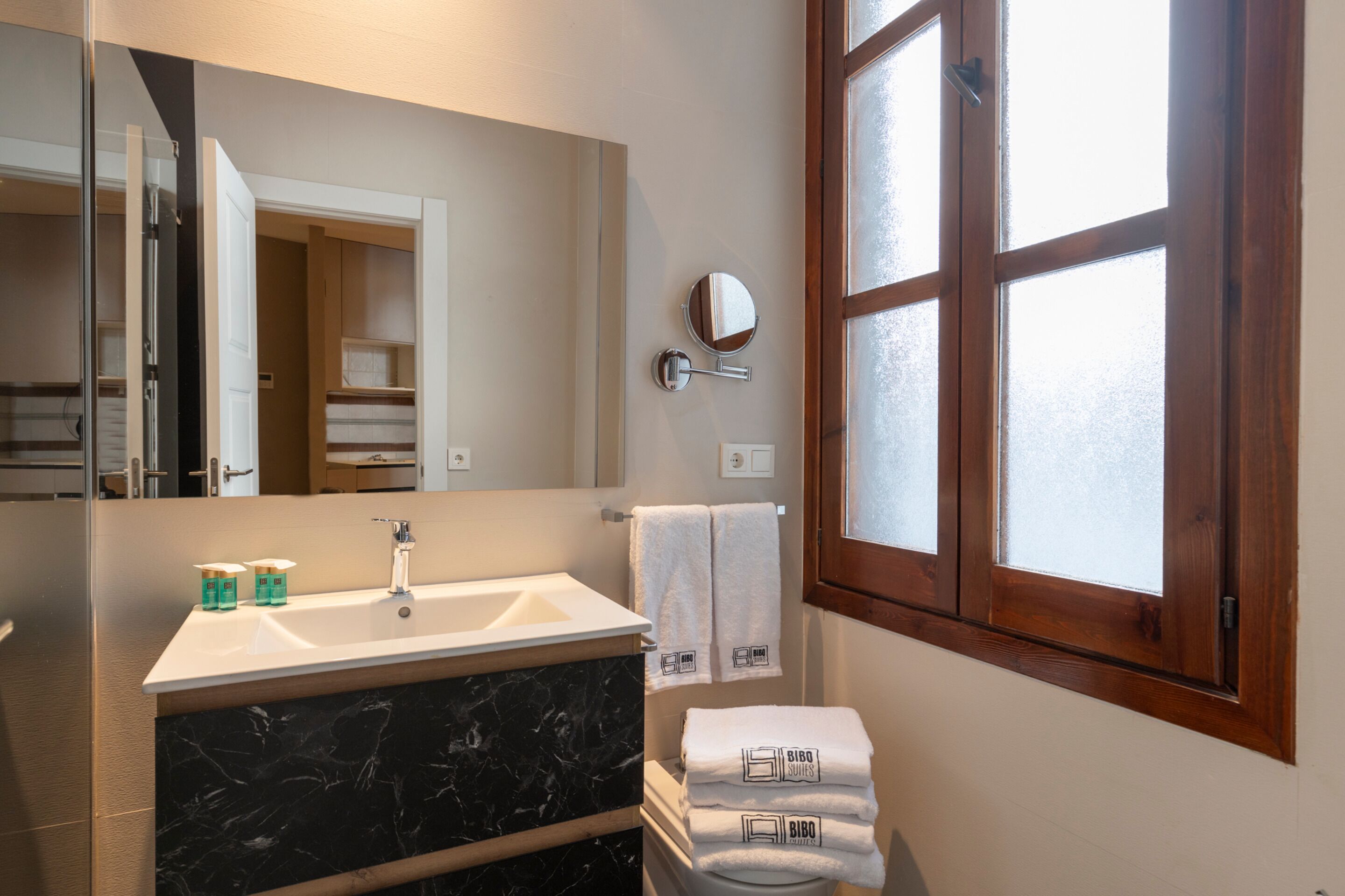 Une salle de bain moderne avec un grand miroir, un lavabo doté d’un plan de toilette en marbre et une fenêtre en verre dépoli.