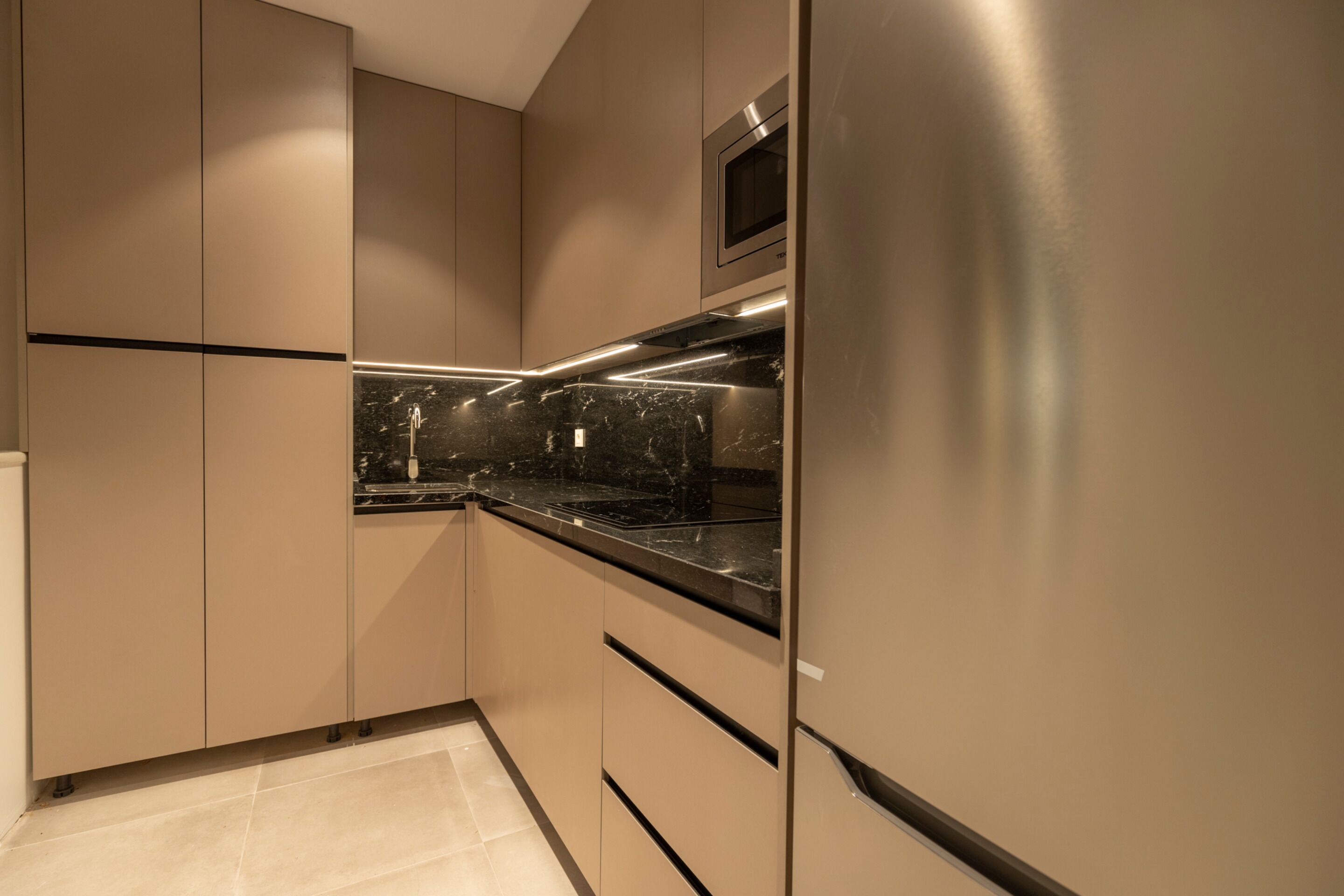 Una cocina moderna con electrodomésticos de acero inoxidable, encimera de mármol y armarios color beige.