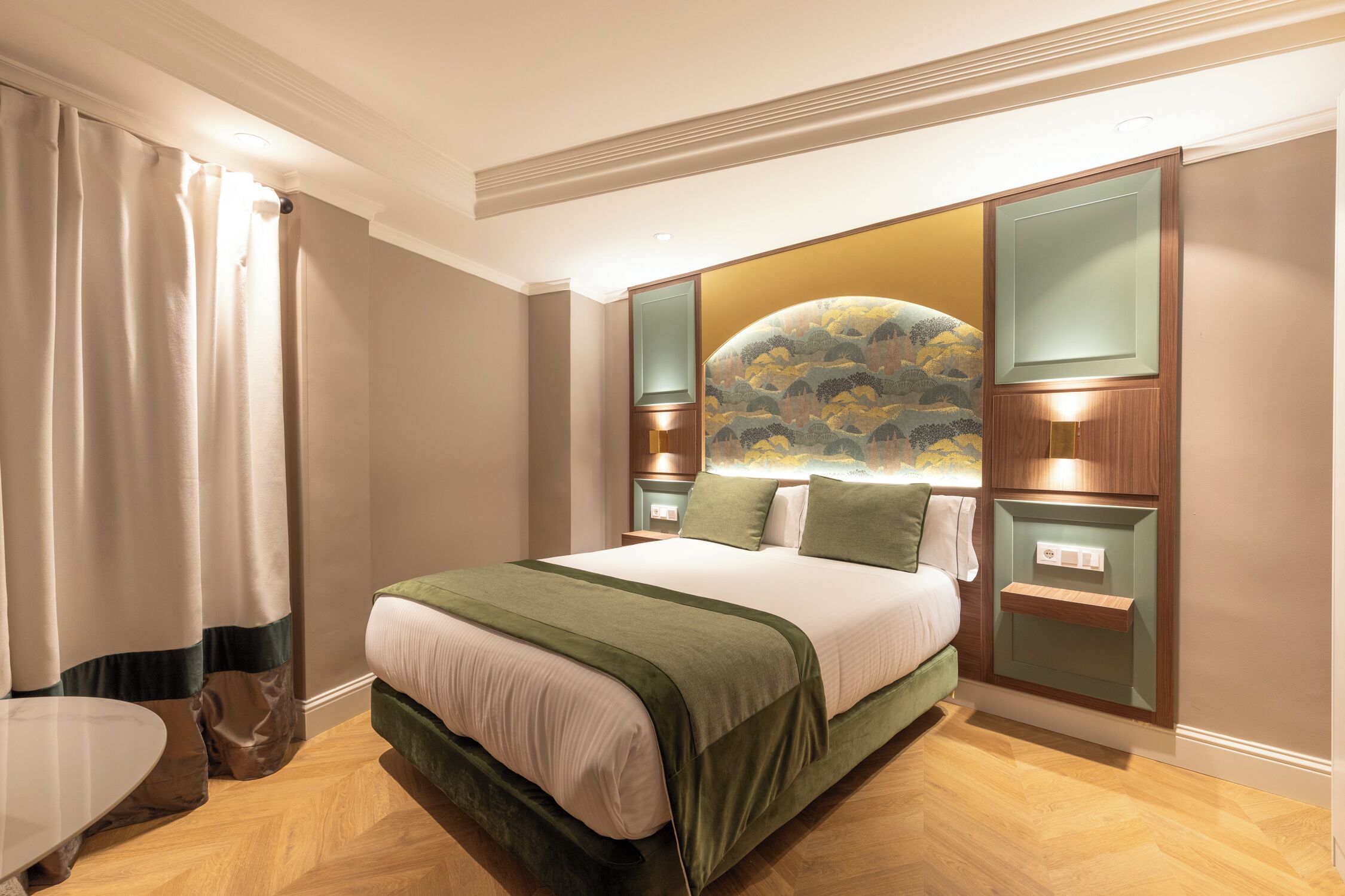 Een hotelkamer met een groot bed, een nachtkastje, een wandplank en een raam met gordijnen.