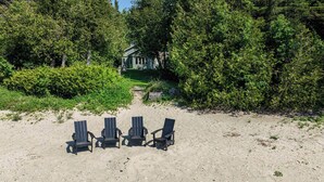 A beach with four chairs facing a house surrounded by dense greenery. - Huron Shores, Hot Tub, Lakefront (Point Clark)